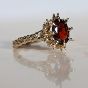 9x7mm oval cut deep red garnet gemstone set into spiked yellow gold prongs, side view of ring.