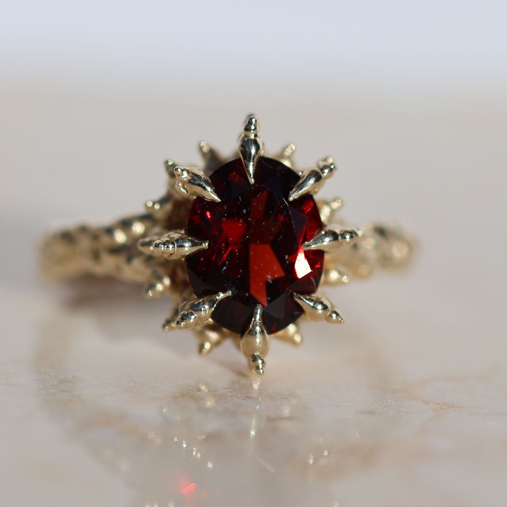 9x7mm oval cut deep red garnet gemstone set into spiked yellow gold prongs, front facing ring.
