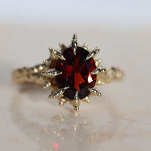 9x7mm oval cut deep red garnet gemstone set into spiked yellow gold prongs, front facing ring.